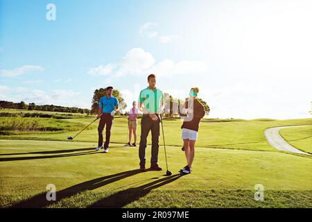Golf ist ein tolles Spiel, um mit anderen Paaren zu spielen. Zwei Paare, die an einem sonnigen Tag eine Runde Golf spielen. Stockfoto