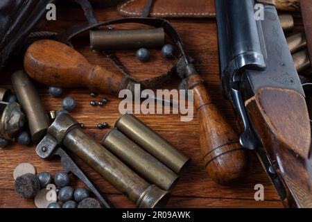 Antike 16-Gauge Break-Action glatt gebohrte Schrotflinte mit Messinggehäuse und Zubehör für Patronennachladung auf Holztisch. Stockfoto