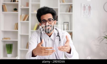 Intelligenter, freundlicher indischer Kliniker im weißen Kittel mit Laptop für die Patientenberatung in der Krankenhauspraxis. Telemedizin. Online-Terminvereinbarung Stockfoto