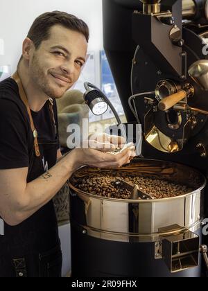 Caen, Frankreich, Mai 2023. Kaffeerösten – ein Mann, der an einer Kaffeeröstermaschine arbeitet, hält Kaffee in der Hand und prüft seine Qualität Stockfoto