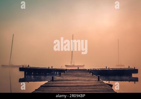 Nebeliger Morgen auf dem See. Boote und Holzpier am Parpocany-See in Tychy, Polen. Stockfoto