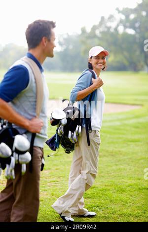 Eine Frau mit Golftasche. Konzentriere dich auf eine lächelnde Frau, die eine Golftasche trägt und den Mann ansieht. Stockfoto