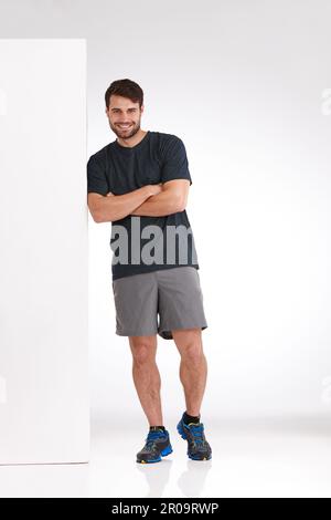 Ich fühle mich entspannt bei meinen Entscheidungen. Studiofoto eines lächelnden jungen Mannes, der sich zwanglos gegen eine leere Plakatwand lehnt. Stockfoto