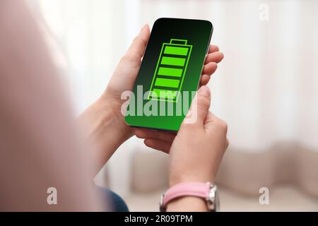 Junge Frau, die ein Smartphone mit voll aufgeladenem Akku in der Hand hält, in Innenräumen, Nahaufnahme Stockfoto