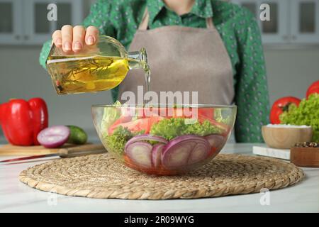 Eine Frau, die Öl aus der Glasflasche in eine Schüssel mit Salat in der Küche gießt, Nahaufnahme Stockfoto