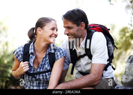 Ich bin so froh, dass wir uns für diese Wanderung entschieden haben. Attraktives, weißes Paar, das Rucksäcke trägt und draußen sitzt. Stockfoto