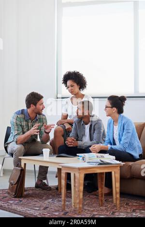 Einen Ideenaustausch. Eine vielfältige Gruppe junger Designer, die sich unterhalten, während sie auf dem Sofa in einem Büro sitzen. Stockfoto