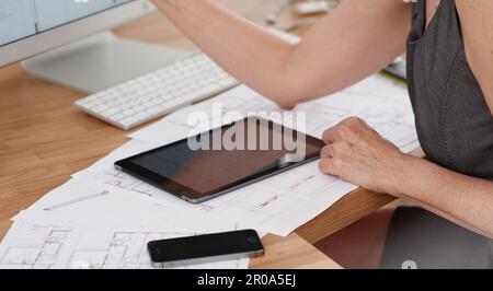 Erstellung detaillierter Blaupausen mithilfe von Technologie. Eine Architektin, die Pläne mit ihrem digitalen Tablet und Computer erstellt. Stockfoto