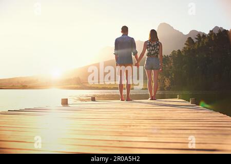 Liebe unter einem wunderschönen Sonnenuntergang. Rückblick auf ein liebevolles junges Paar, das bei Sonnenuntergang auf einem Dock steht. Stockfoto
