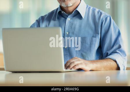 Gesichtsloses Bild einer Person mit einem Spitzbart, die einen Laptop im Freien benutzt. Das ist ein Mann mittleren Alters, der ein Jeansshirt trägt. Stockfoto