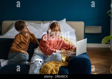 Kinder Teenager Mädchen mit Kopfhörern und Junge lernen Online-Kurs auf einem Laptop, der zu Hause auf dem Sofa sitzt. Stockfoto