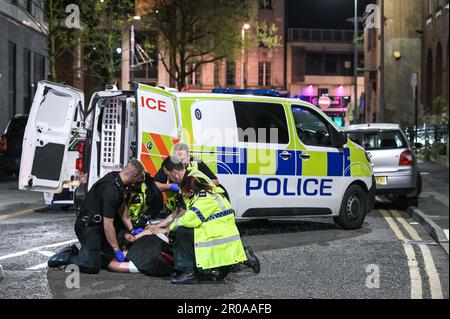 Broad Street, Birmingham, 8. Mai 2023 - die Polizei von West Midlands musste diesen Mann zu Boden ringen, nachdem er sich nach einem Vorfall in einem Nachtclub der Verhaftung widersetzte. Am Sonntagabend stiegen Reveller auf die Broad Street von Birmingham für eine königliche Afterparty ab. Die Polizei war auch bei mehreren anderen Vorfällen entlang des berüchtigten Streifens dabei, als temperiert wurde. Eine Frau wurde von einem Sanitäter in einen Krankenwagen gefahren, der einen Krankenwagen hielt. Die meisten Feiernden trugen normale Wochenend-Outfits, aber einige hielten sich immer noch an den Feierlichkeiten fest, die Union Flag Hüte und König Karl III Masken und große Ohren trugen. Der Partygänger Stockfoto