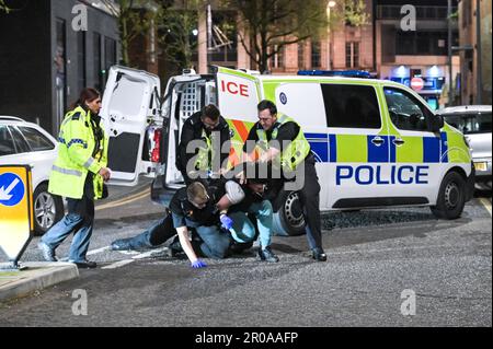 Broad Street, Birmingham, 8. Mai 2023 - die Polizei von West Midlands musste diesen Mann zu Boden ringen, nachdem er sich nach einem Vorfall in einem Nachtclub der Verhaftung widersetzte. Am Sonntagabend stiegen Reveller auf die Broad Street von Birmingham für eine königliche Afterparty ab. Die Polizei war auch bei mehreren anderen Vorfällen entlang des berüchtigten Streifens dabei, als temperiert wurde. Eine Frau wurde von einem Sanitäter in einen Krankenwagen gefahren, der einen Krankenwagen hielt. Die meisten Feiernden trugen normale Wochenend-Outfits, aber einige hielten sich immer noch an den Feierlichkeiten fest, die Union Flag Hüte und König Karl III Masken und große Ohren trugen. Der Partygänger Stockfoto