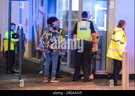 Broad Street, Birmingham, 8. Mai 2023 - Sonntagabend stiegen Reveller auf Birminghams Broad Street ab, um eine königliche Afterparty zu feiern. Die Polizei war auch draußen und musste einen Mann zu Boden ringen, nachdem er sich nach einem Vorfall in einem Nachtclub der Verhaftung widersetzte. Die Polizei war auch bei mehreren anderen Vorfällen entlang des berüchtigten Streifens dabei, als temperiert wurde. Eine Frau wurde von einem Sanitäter in einen Krankenwagen gefahren, der einen Krankenwagen hielt. Die meisten Feiernden trugen normale Wochenend-Outfits, aber einige hielten sich immer noch an den Feierlichkeiten fest, die Union Flag Hüte und König Karl III Masken und großes Ohr trugen Stockfoto