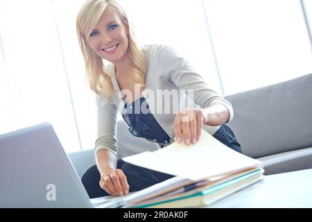 Ich arbeite hart für mein Geld. Porträt einer wunderschönen Blondine, die mit einem Laptop vor ihr durch die Akten geht - Copyspace. Stockfoto