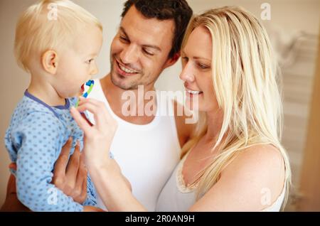 Ich kümmere mich um die Zähne der Kleinen. Eine junge Mutter und ein junger Vater, die ihren kleinen Jungen die Zähne putzen. Stockfoto