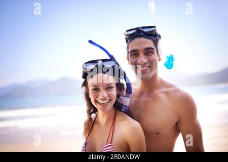 Gehen wir runter. Ein glückliches junges Paar in Schnorchelausrüstung am Strand. Stockfoto