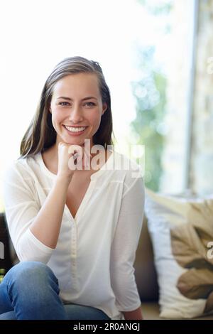 Sie kann einen Raum mit diesem Lächeln aufhellen. Ein Porträt einer glücklichen und sorglosen jungen Frau, die zu Hause auf dem Sofa sitzt. Stockfoto