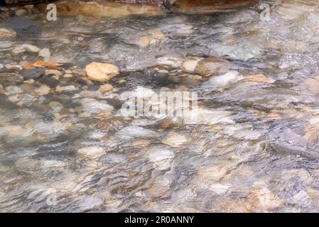 Ein flaches Flussbett im Frühling mit klarem, unberührtem Wasser, das über große Felsen und Steine unter der Wasseroberfläche fließt. Stockfoto