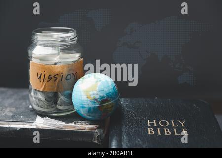 Spargläser voller Geld und Globus mit heiliger Bibel für Mission, Mission christian Idea. bibel und Buch auf Holztisch, christlicher Hintergrund für Gre Stockfoto