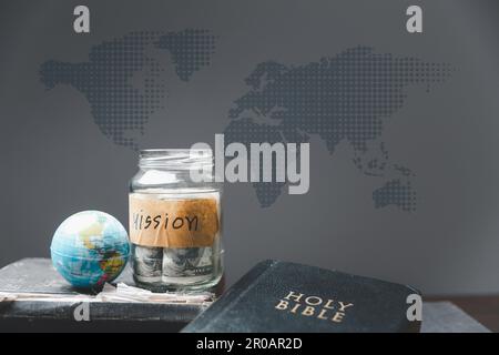 Spargläser voller Geld und Globus mit heiliger Bibel für Mission, Mission christian Idea. bibel und Buch auf Holztisch, christlicher Hintergrund für Gre Stockfoto