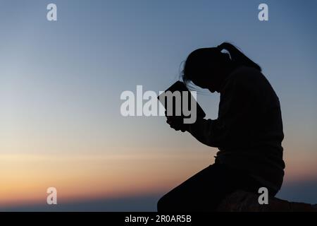 Silhouette einer Frau, die im Himmelshintergrund um Gottesverehrung betet. Christen beten zu jesus christus um Ruhe. Am Morgen kamen die Leute zu A Stockfoto