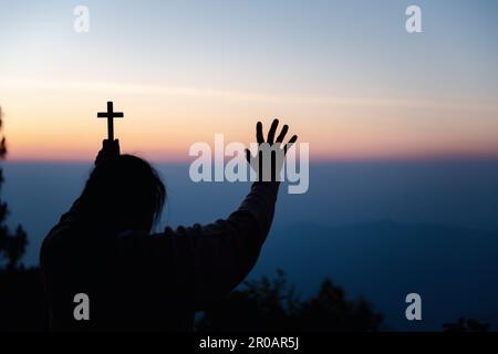 Silhouette einer Frau, die im Himmelshintergrund um Gottesverehrung betet. Christen beten zu jesus christus um Ruhe. Am Morgen kamen die Leute zu A Stockfoto