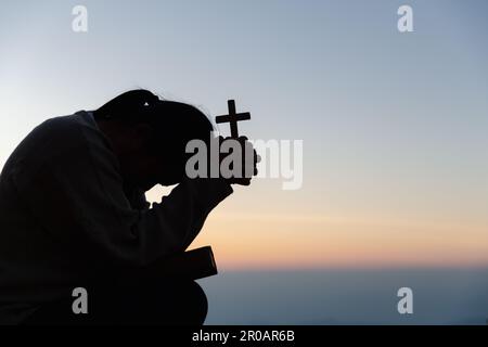 Silhouette einer Frau, die im Himmelshintergrund um Gottesverehrung betet. Christen beten zu jesus christus um Ruhe. Am Morgen kamen die Leute zu A Stockfoto