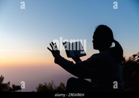 Silhouette einer Frau, die im Himmelshintergrund um Gottesverehrung betet. Christen beten zu jesus christus um Ruhe. Am Morgen kamen die Leute zu A Stockfoto