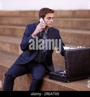 Multitasking wie ein Profi in der Stadt. Ein Geschäftsmann, der telefoniert, während er mit seiner Aktentasche auf einer Treppe sitzt. Stockfoto