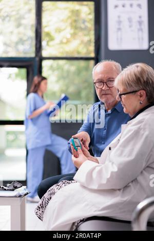 Älterer Arzt, der den Insulinspiegeltest des Patienten mit dem Glukometer im Wartezimmer des Krankenhauses durchführt, Diabetesuntersuchung zur Blutzuckermessung. Älterer Mann mit Arztbesuch Stockfoto