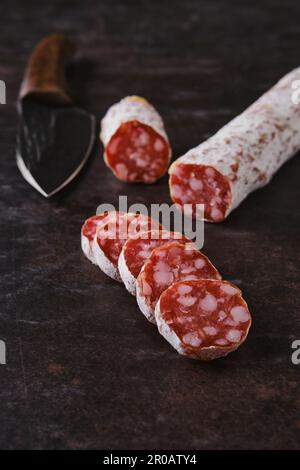 Scheiben fermentierter Salami-Würste auf dunklem Hintergrund Stockfoto