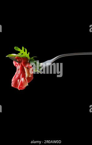 Ein Stück Marmorfleisch-Carpaccio auf einer Gabel auf schwarzem Hintergrund Stockfoto