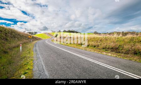 Kurvenreiche, leere Straße, die in der Wintersaison bergauf durch Adelaide Hills Ackerland führt, Südaustralien Stockfoto