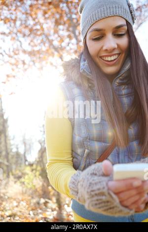 Den Moment mit ihrer Familie und ihren Freunden zu teilen. Eine wunderschöne junge Frau, die mit ihrem Smartphone draußen steht. Stockfoto