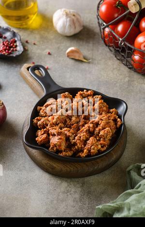 Hackfleisch und Tomaten-Bolognese-Sauce, in einer schwarzen Pfanne, neben den Zutaten für Pasta, Spaghetti, Parmesankäse Hochwertiges Foto Stockfoto