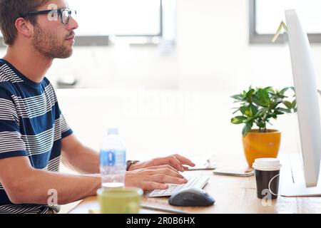 Auf seine eigenen beruflichen Ziele hinarbeiten. Zugeschnittenes Profilbild eines jungen Profis, der an seinem pc in einem hellen Büro arbeitet. Stockfoto
