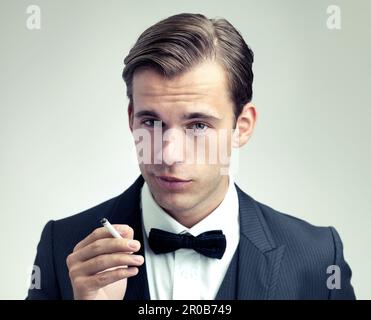 Ein Mann von Raffinesse. Ein abgeschnittenes Porträt eines selbstbewussten jungen Mannes, der eine Zigarette raucht. Stockfoto