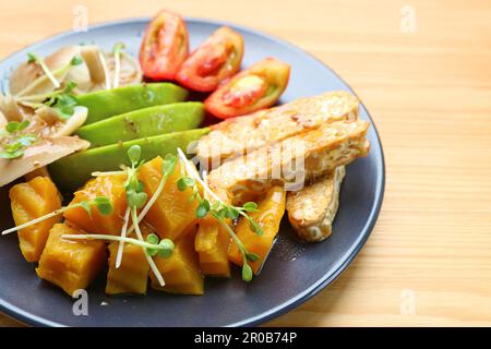 Teller mit gebratenem Tempeh und farbenfrohem Gemüsesalat garniert mit Daikon-Sprossen Stockfoto