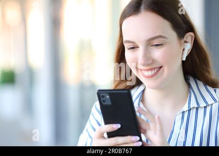 Glückliche Frau, die auf der Straße Musik mit Ohrstöpseln und Telefon hört Stockfoto