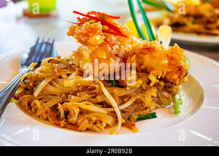 Pad thai-Reisnudeln mit frittierten Garnelen oder Garnelen und Gemüse in weißer Keramikplatte auf Holztisch. Stockfoto