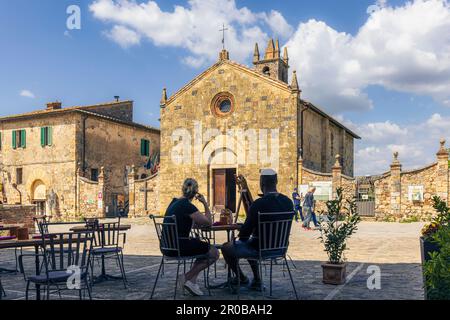 Monteriggioni, Provinz Siena, Toskana, Italien. Ein Paar genießt einen Drink vor der romanisch-gotischen Kirche Santa Maria aus dem 13. Jahrhundert. Stockfoto