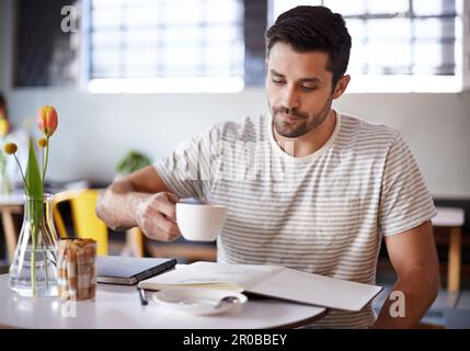 Zeit, sich zu konzentrieren. Ein gutaussehender junger Mann, der Kaffee trinkt, während er mit seinem Notizbuch in einem Restaurant sitzt. Stockfoto
