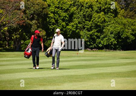 Wer braucht einen Caddy, wenn dein Kumpel neben dir läuft? Zwei Männer, die ihre Golftaschen über einen Golfplatz tragen. Stockfoto