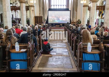 Die Leute saßen in der St.-Michaels-Kirche Framlingham Suffolk und sahen die Krönung von König Karl III. Auf einem großen Fernsehbildschirm Stockfoto