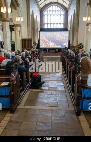 Die Leute saßen in der St.-Michaels-Kirche Framlingham Suffolk und sahen die Krönung von König Karl III. Auf einem großen Fernsehbildschirm Stockfoto