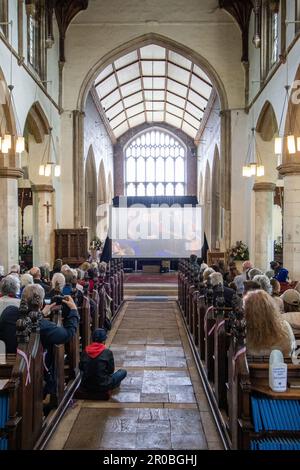 Die Leute saßen in der St.-Michaels-Kirche Framlingham Suffolk und sahen die Krönung von König Karl III. Auf einem großen Fernsehbildschirm Stockfoto