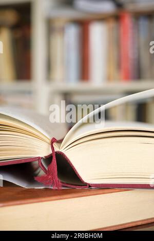 Offenes Buch oder Lehrbuch auf einem Stapel geschlossener Bücher vor einem Bücherregal in einer Bibliothek. Lernkonzept im Bildungsbereich. Vertikales Bild mit selektivem Fokus. Stockfoto