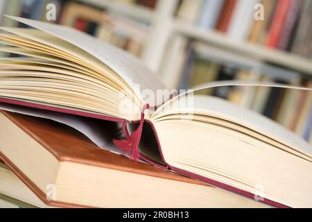 Offenes Buch oder Lehrbuch auf einem Stapel geschlossener Bücher vor einem Bücherregal in einer Bibliothek. Lernkonzept im Bildungsbereich. Bild mit selektivem Fokus. Stockfoto