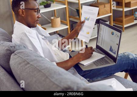 Junger afroamerikanischer Unternehmer, der sich mit Geschäftsforschung beschäftigt und einen Laptop benutzt Stockfoto